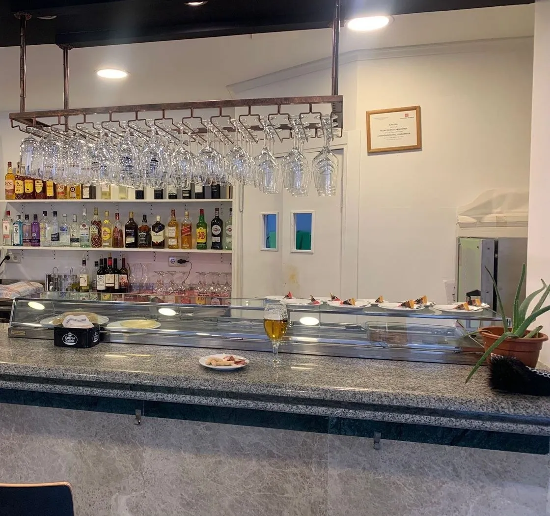 Barra de granito con botellas, copas colgadas, un vaso de cerveza y tapas en la vitrina