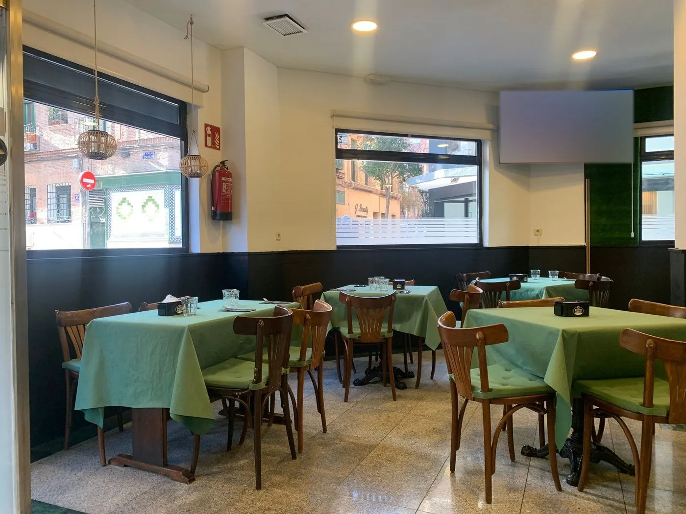 Comedor con mesas de mantel verde, sillas de madera y ventanales a la calle