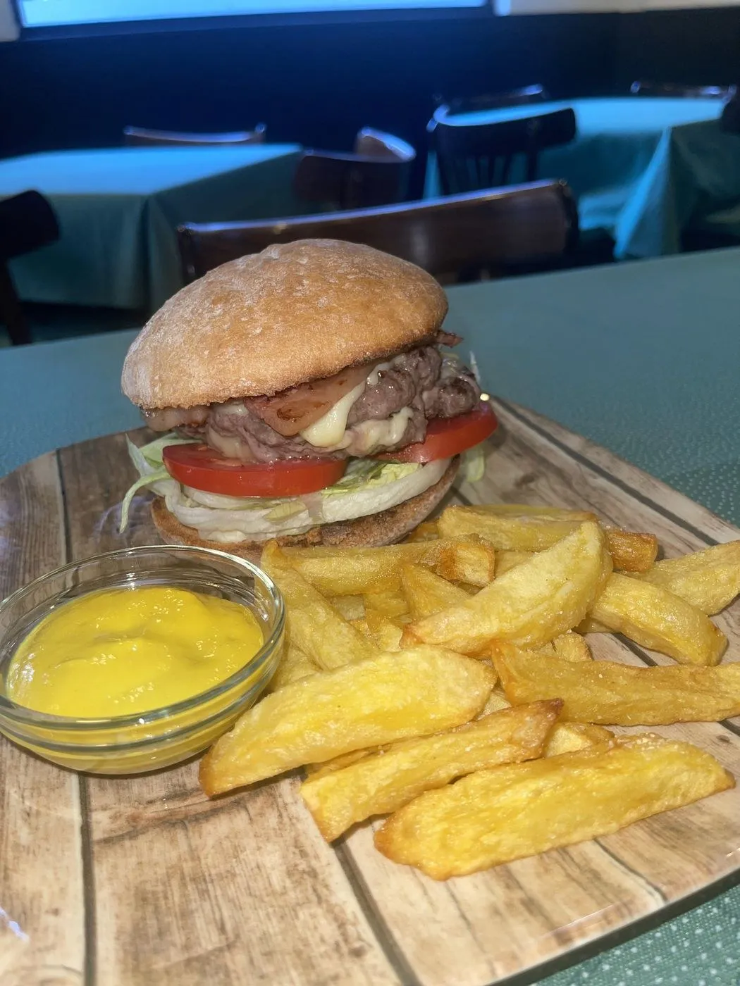 Hamburguesa con queso, beicon y tomate, con patatas fritas y una salsa amarilla
