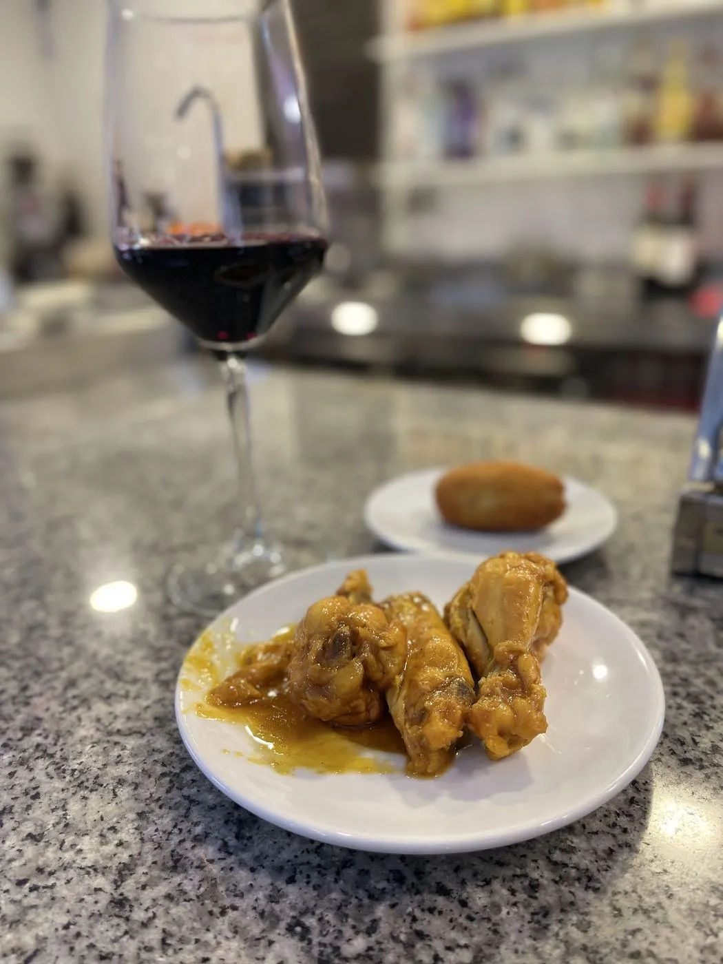 Plato de alitas de pollo en salsa con una copa de vino tinto en la barra