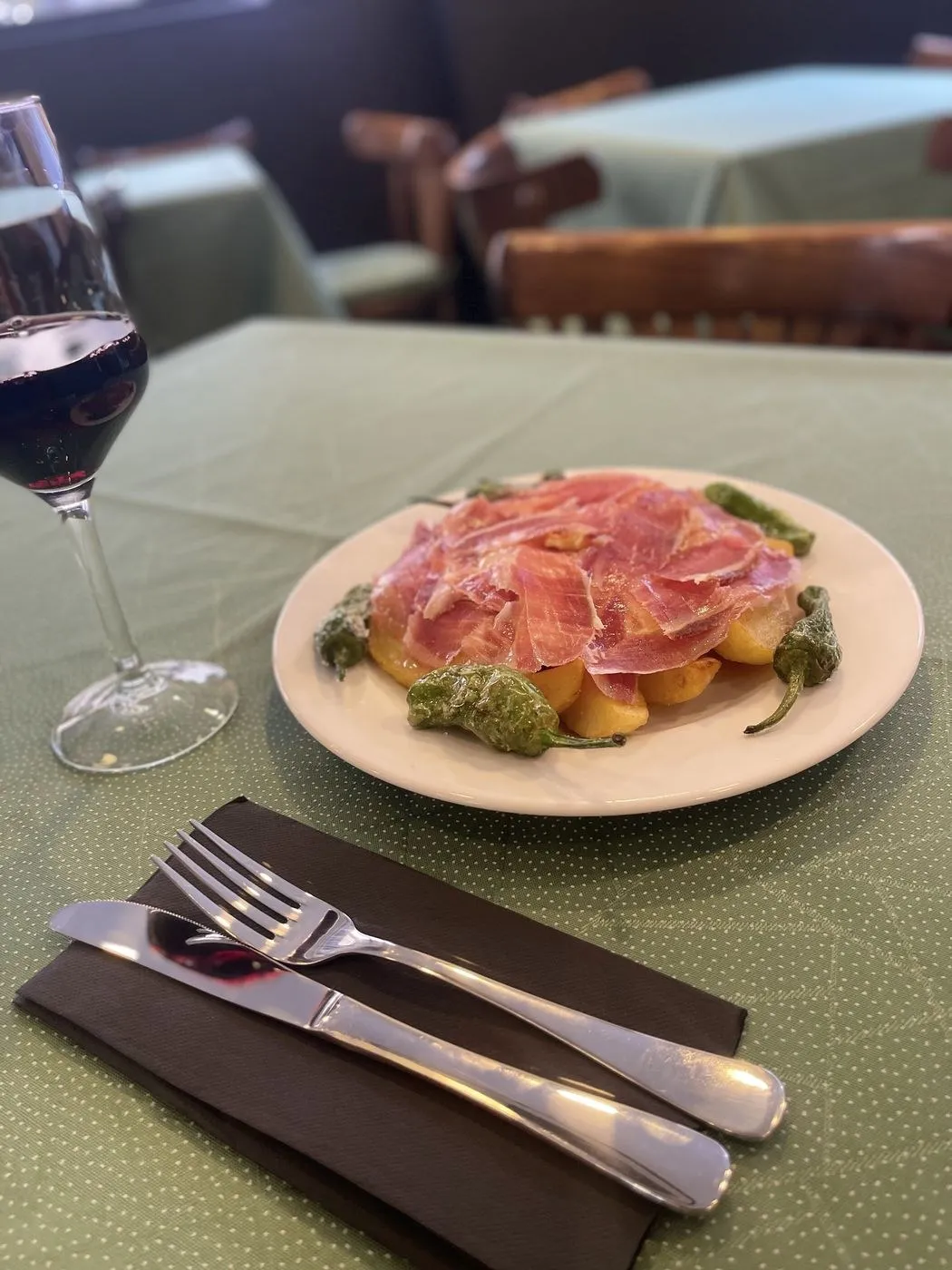 Plato de jamón sobre patatas con pimientos de Padrón y una copa de vino tinto