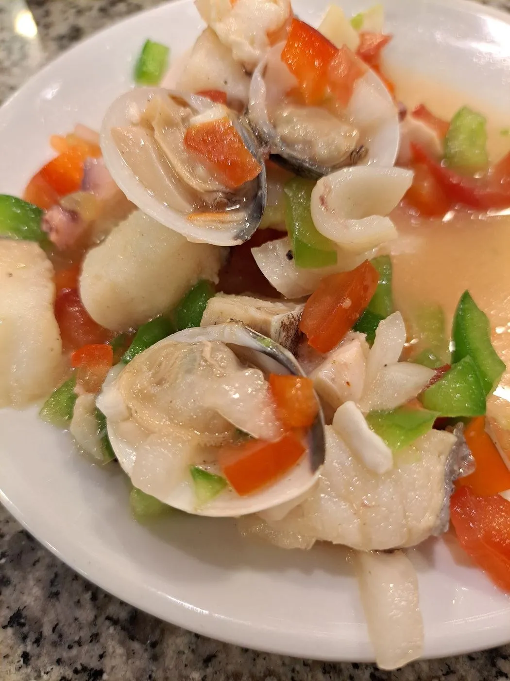 Salpicón de marisco con almejas, pescado y pimiento troceado en un plato blanco
